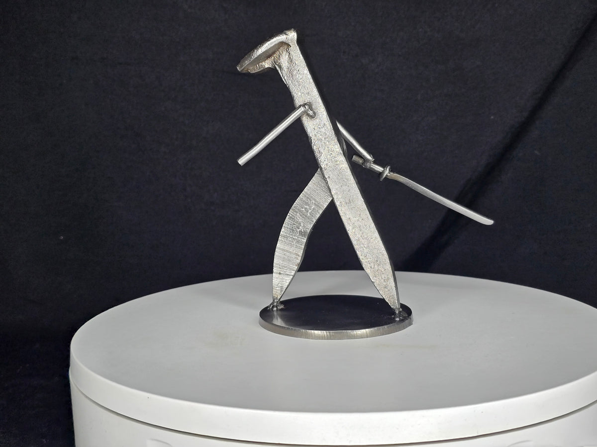 The Martial Artist handcrafted railroad spike sculpture posed with a steel sword in a forward-moving martial arts stance.
