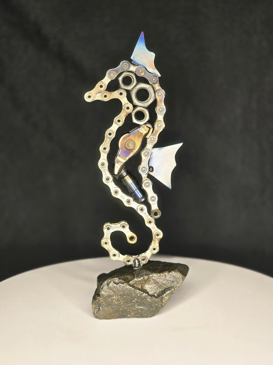 Metal chain horse sculpture with small bottle, mounted on dark stone base