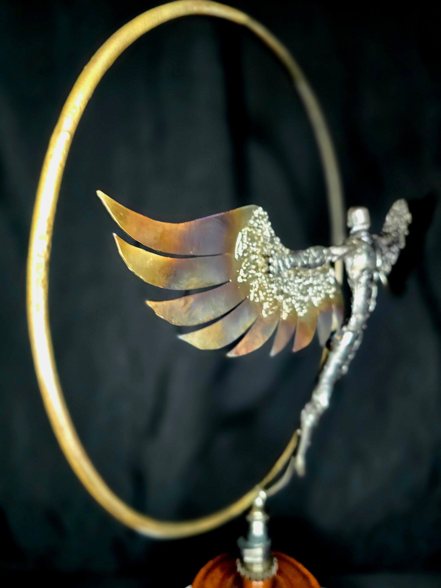 Ikarus: The Day After sculpture by Enrique Del Angel. A winged figure emerges from a golden circle, with heat-colored wings.
