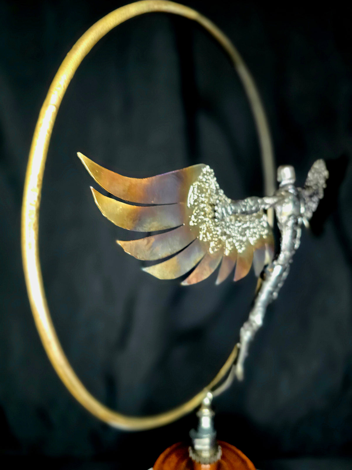 Ikarus: The Day After sculpture by Enrique Del Angel. A winged figure emerges from a golden circle, with heat-colored wings.