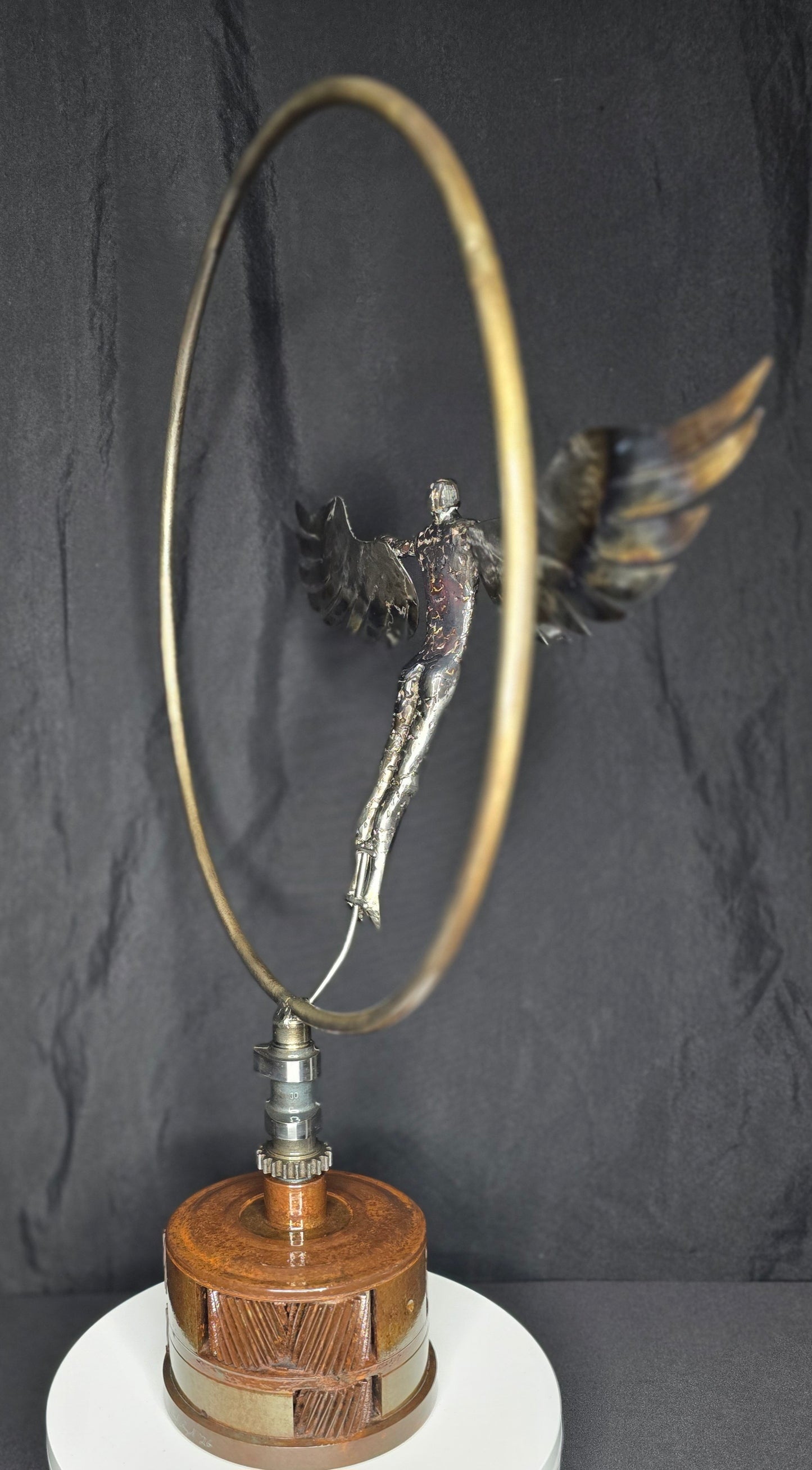 Ikarus: The Day After sculpture by Enrique Del Angel. Metal figure with wings in a hoop, on a wooden base.