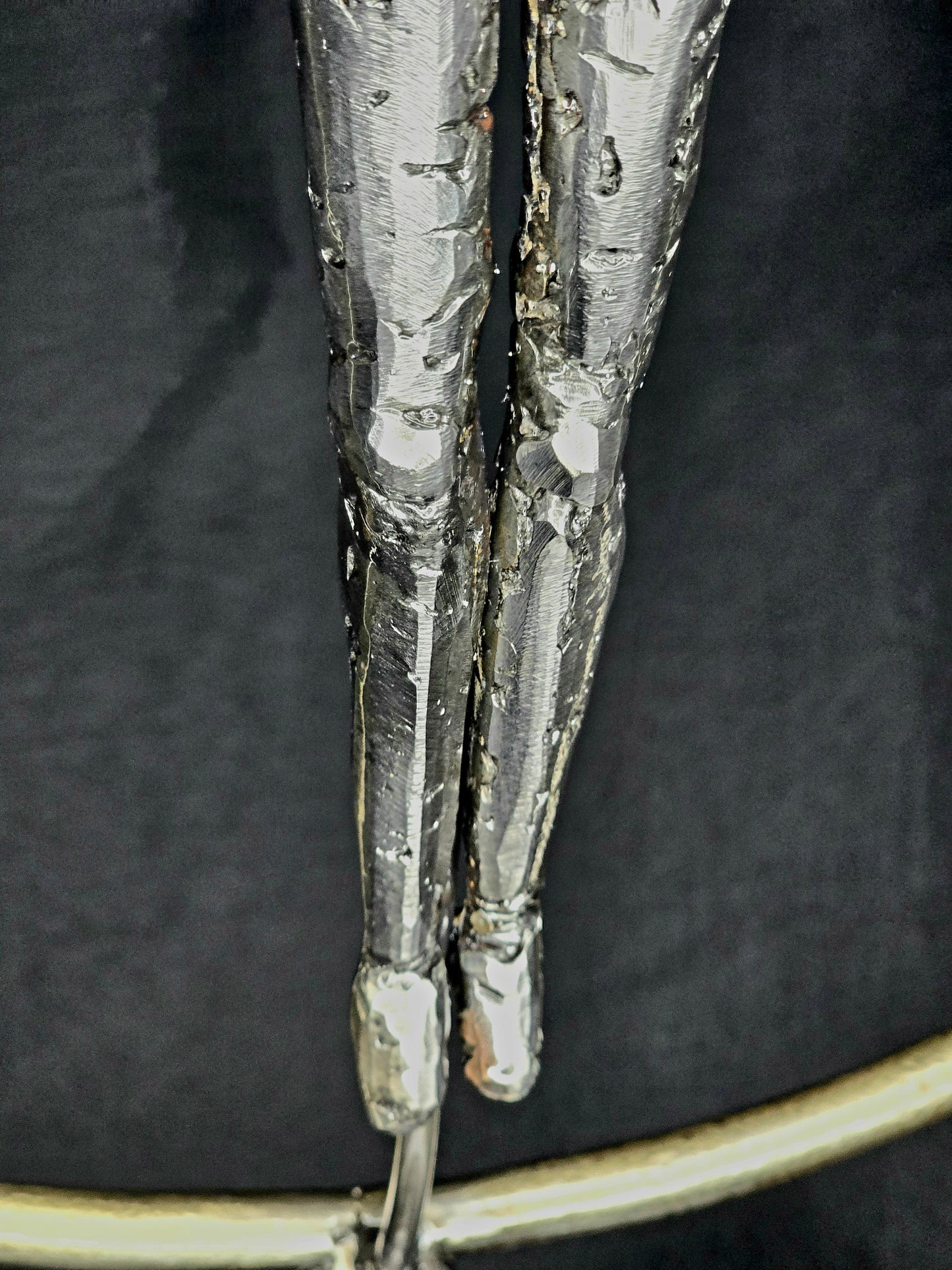 Ikarus: The Day After sculpture by Enrique Del Angel, showing two metallic legs with textured surfaces against a dark background.