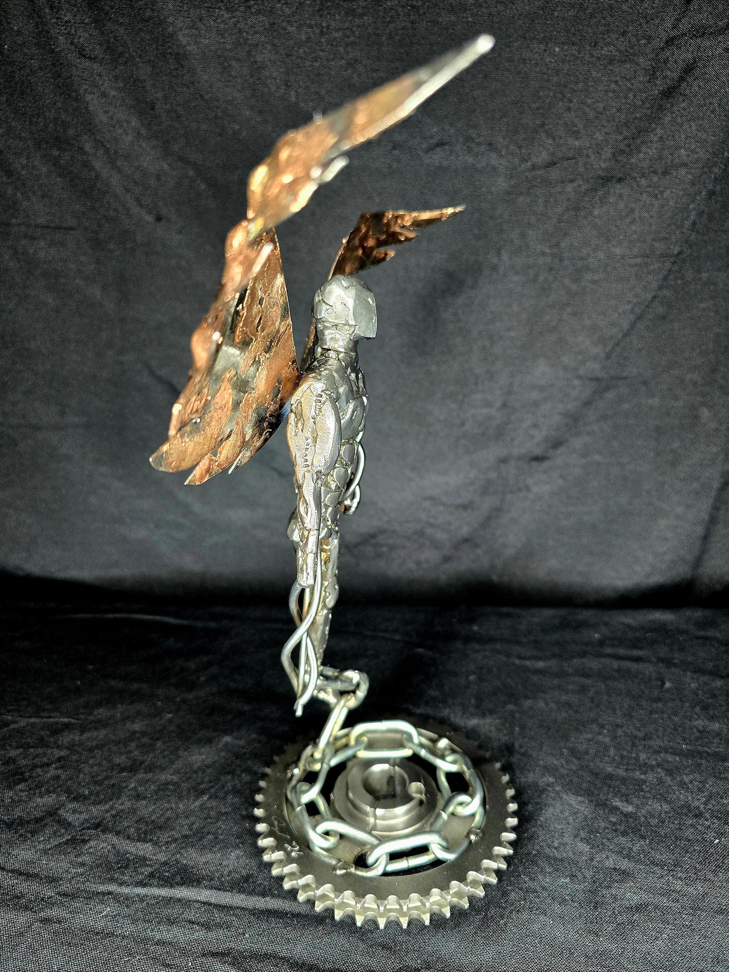Metal angel ornament in profile with gold wings, silver body, and round gear base