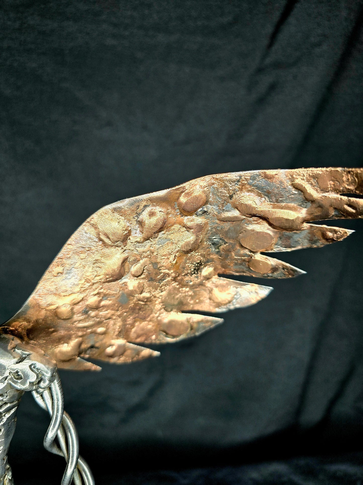 Metal angel ornament close-up showing one gold-toned wing and linked chain