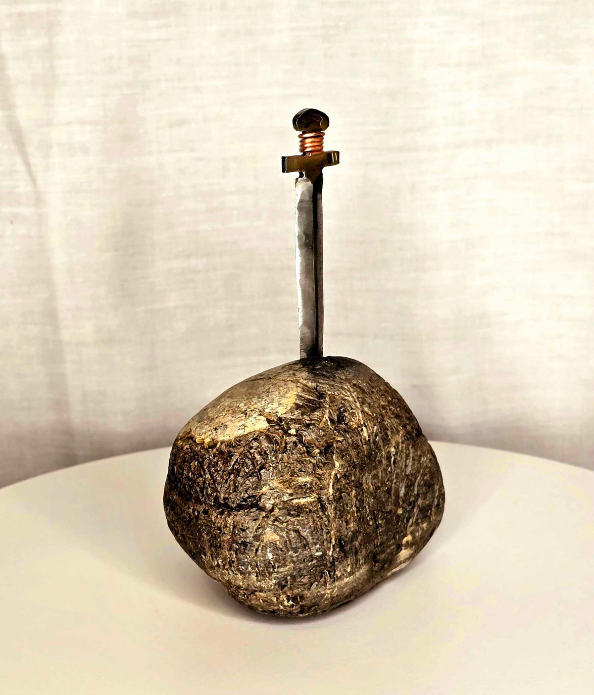 Excalibur sculpture: metal sword with copper wire hilt embedded in a textured rock.