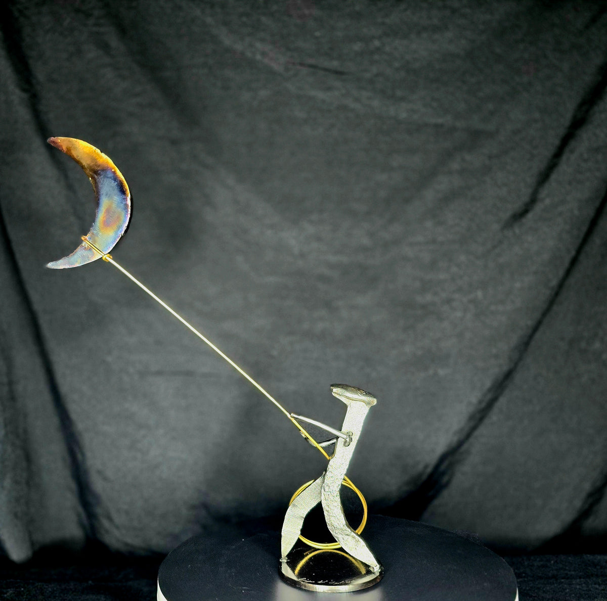 Left view, I Swear: By the Stars and the Moon Above mixed-media metal sculpture by Texas artist Enrique Del Angel, featuring a railroad spike cowboy roping a crescent moon filled with stars.