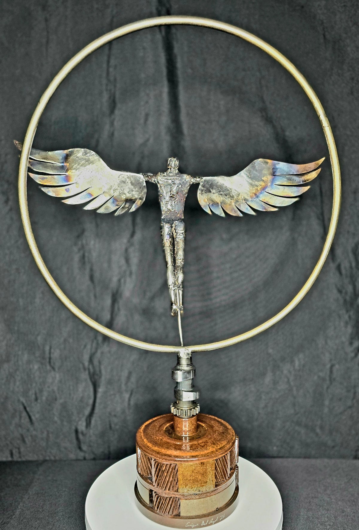 Ikarus: The Day After sculpture by Enrique Del Angel. Metal figure with wings in a circle, on a base.