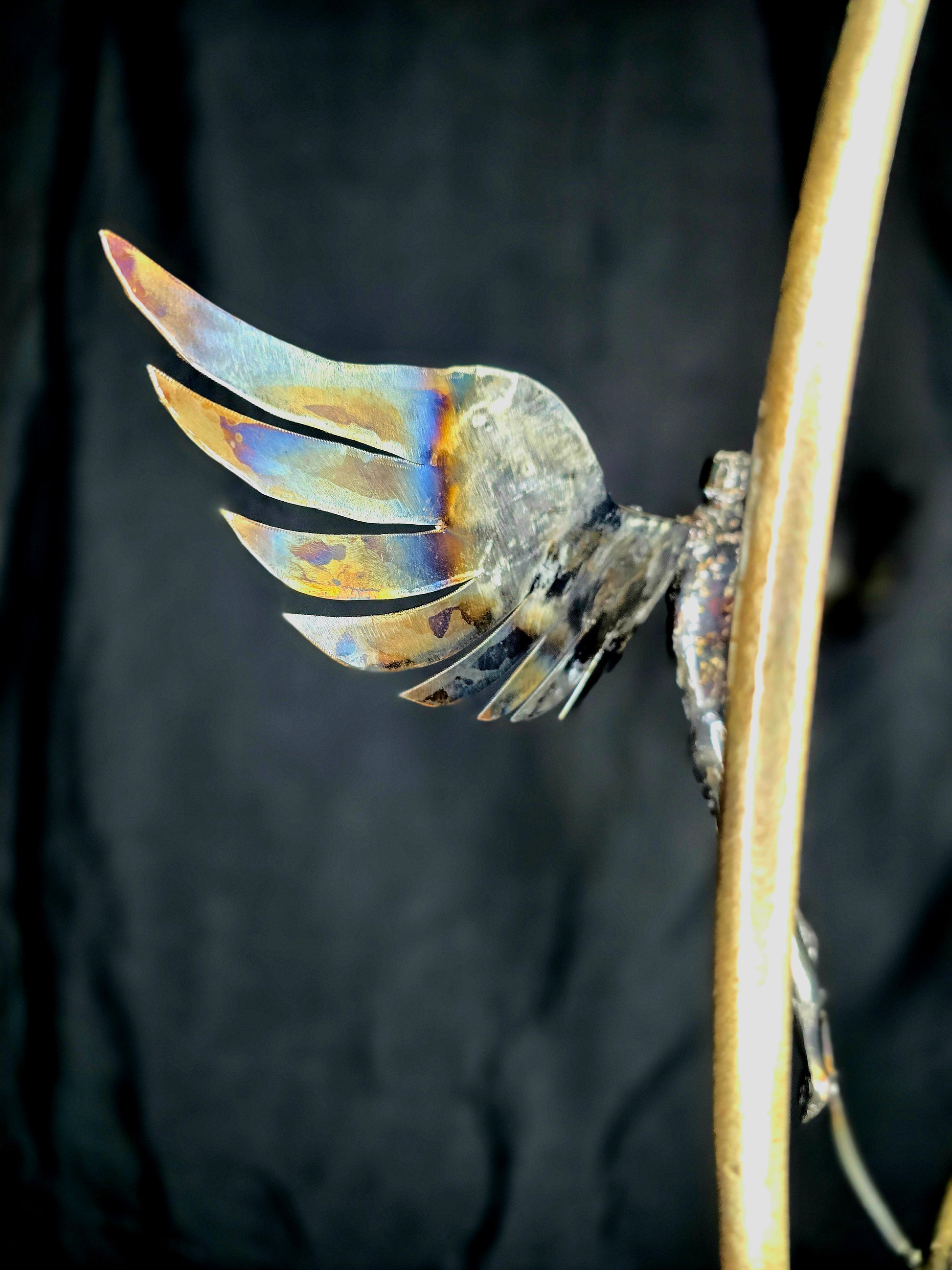 Ikarus: The Day After sculpture by Enrique Del Angel. Metal wing with heat-colored accents on a golden rod.
