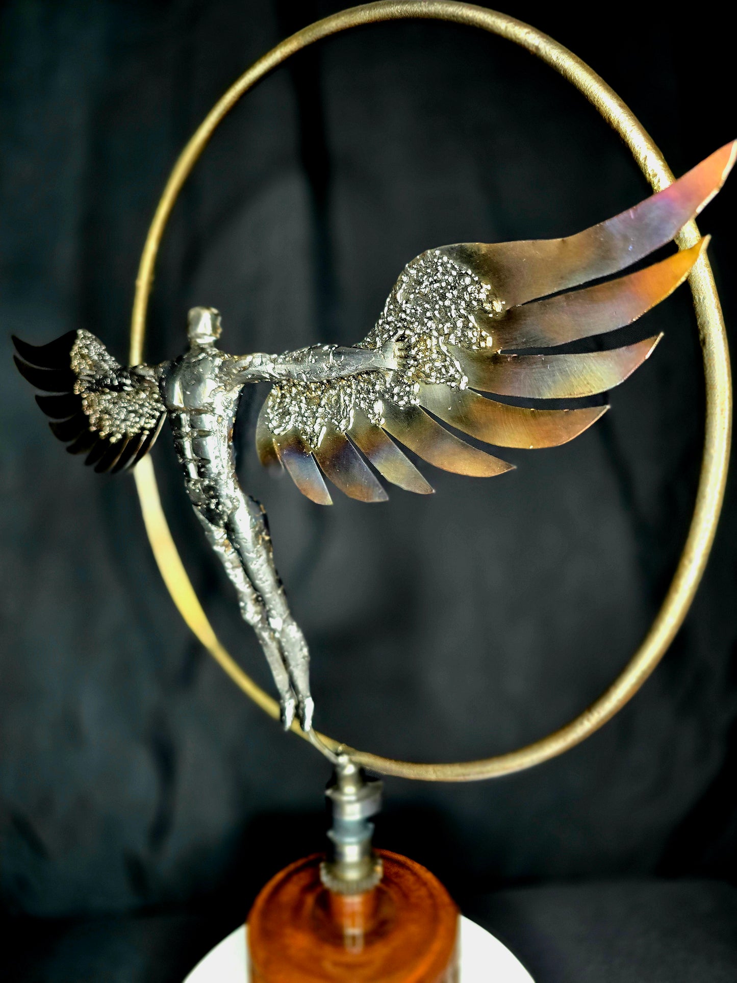 Ikarus: The Day After sculpture by Enrique Del Angel, metal figure with wings in a golden circle.