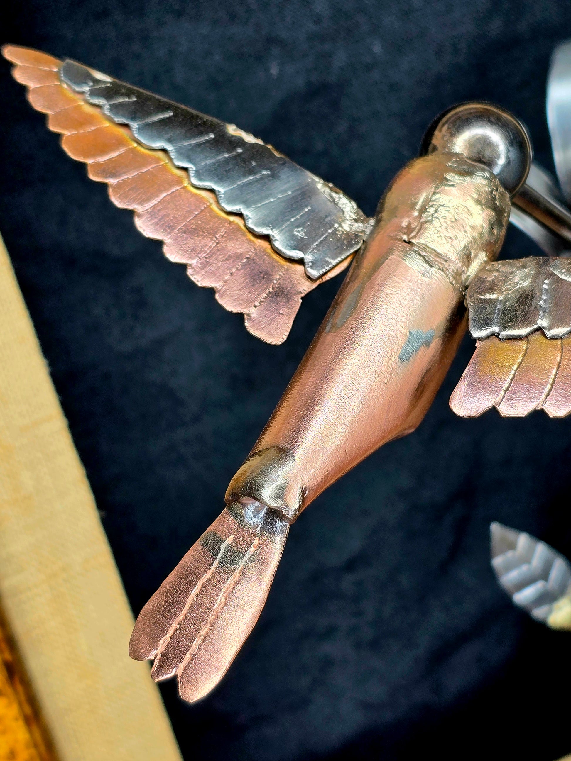 Close-up of metal bird wing feathers and copper body, with silver flower petals