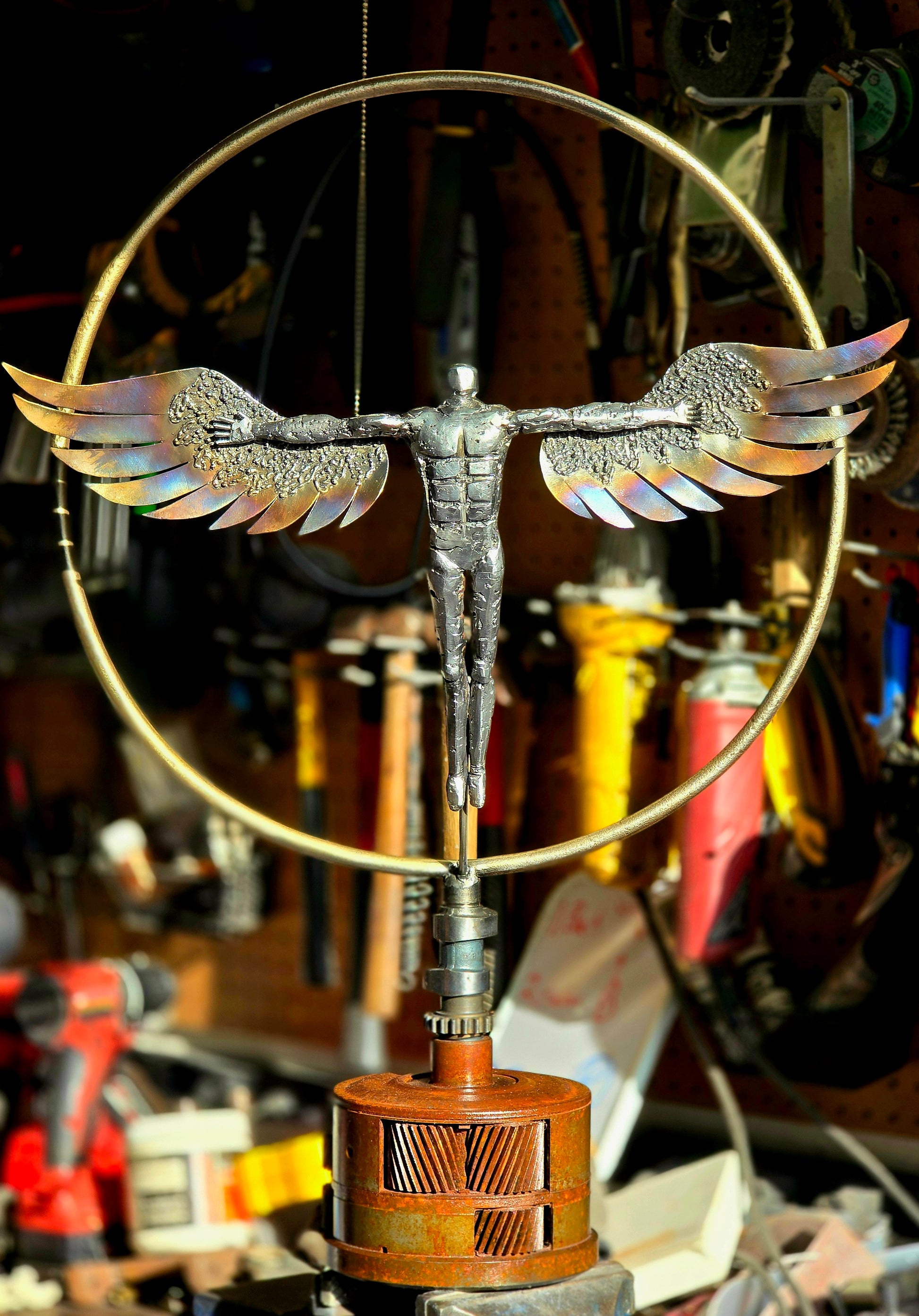 Winged metal figure sculpture with circular frame on a tall pedestal stand