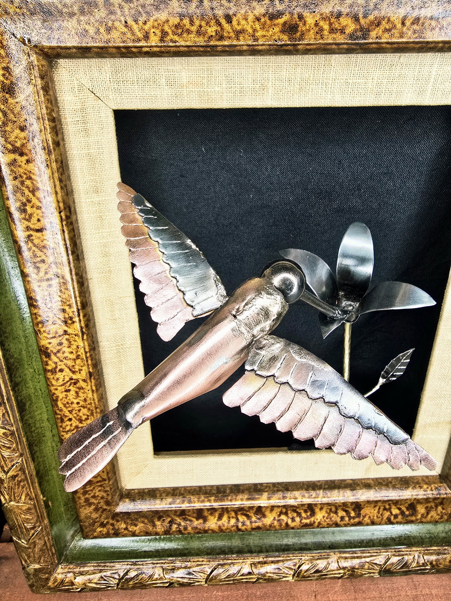Framed metal bird sculpture with copper-and-silver wings and a flower stem