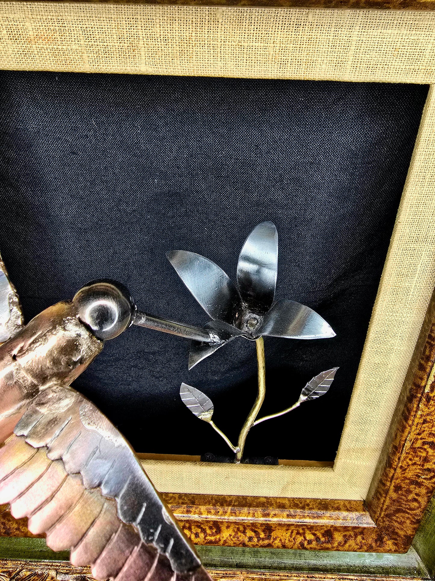 Framed metal bird sculpture side view with copper body, silver wings, and flower stems