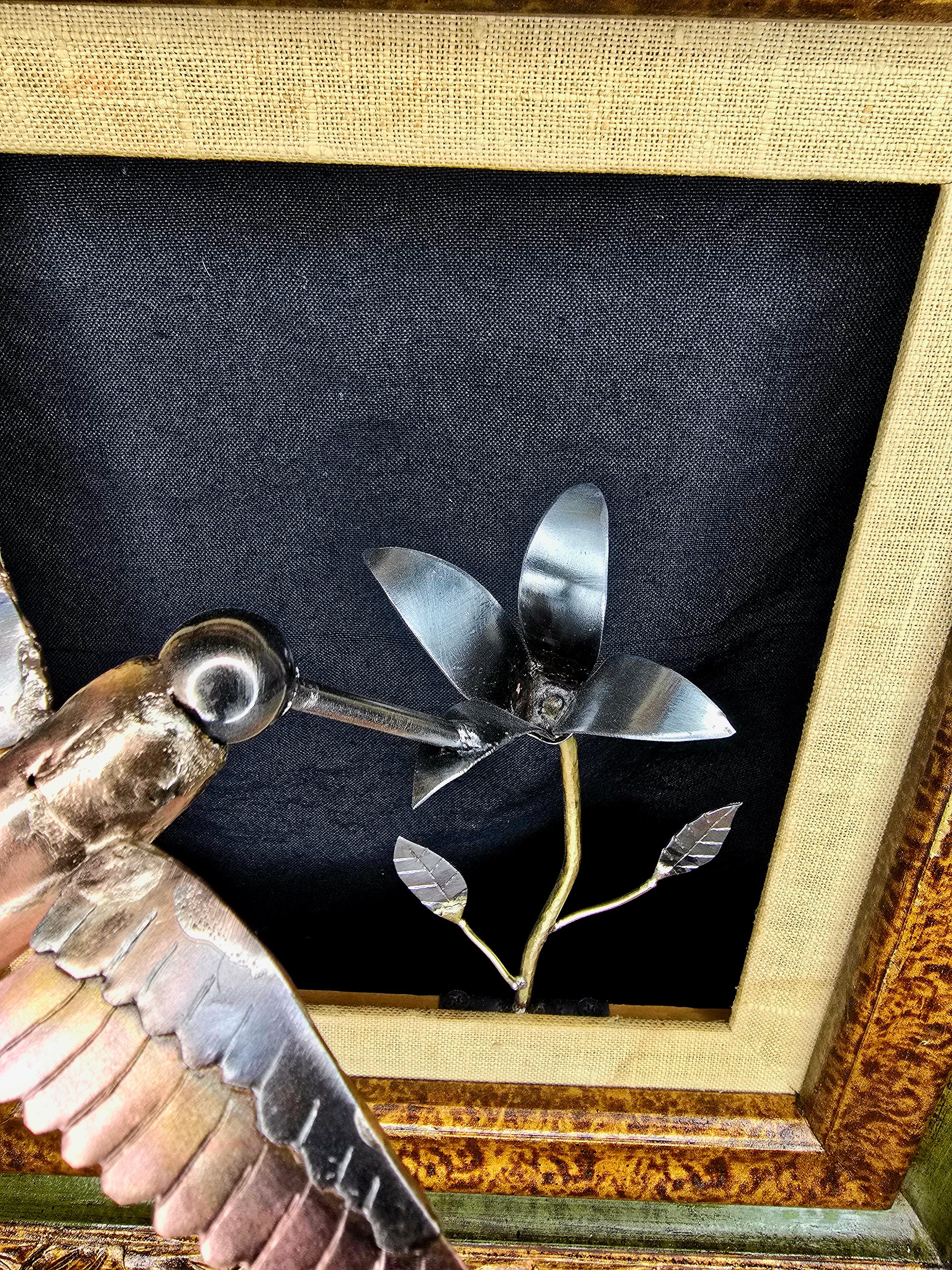 Framed metal bird sculpture side view with copper body, silver wings, and flower stems