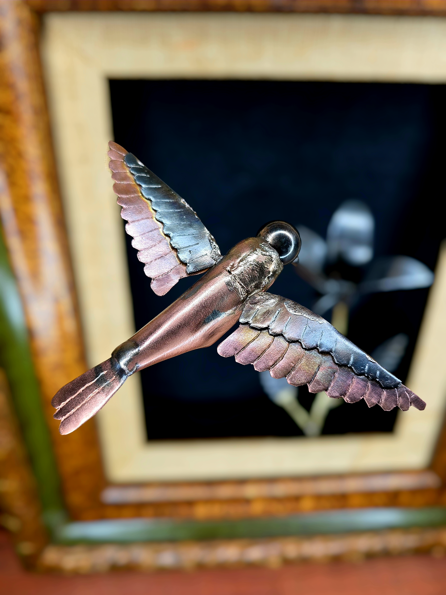 Close-up of framed metal bird sculpture with copper body and layered silver wing feathers