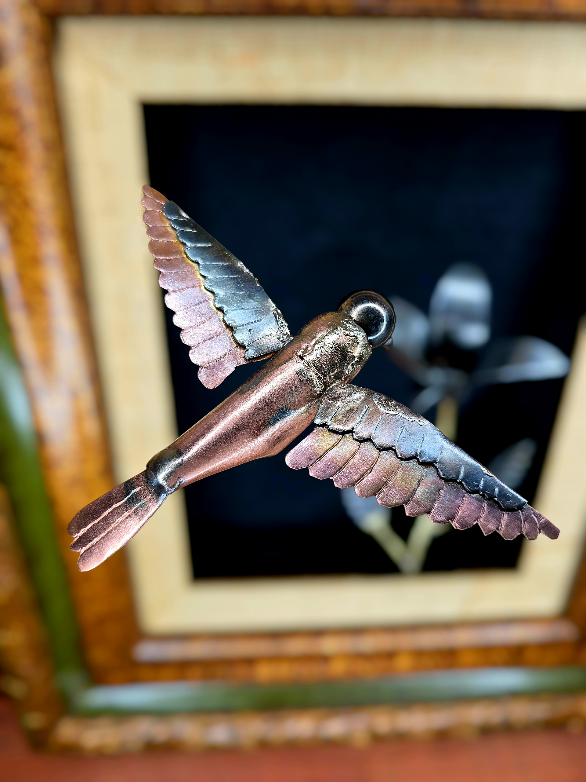 Close-up of framed metal bird sculpture with copper body and layered silver wing feathers