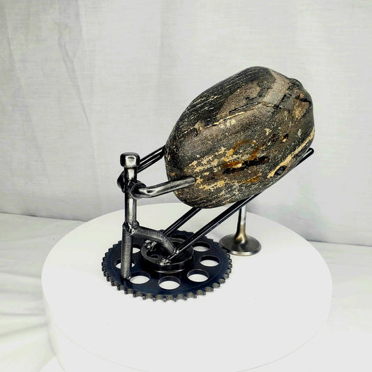 Sisyphus in Motion welded steel figure pushing a natural stone boulder up a gear base sculpture by Enrique Del Angel handcrafted from upcycled auto parts