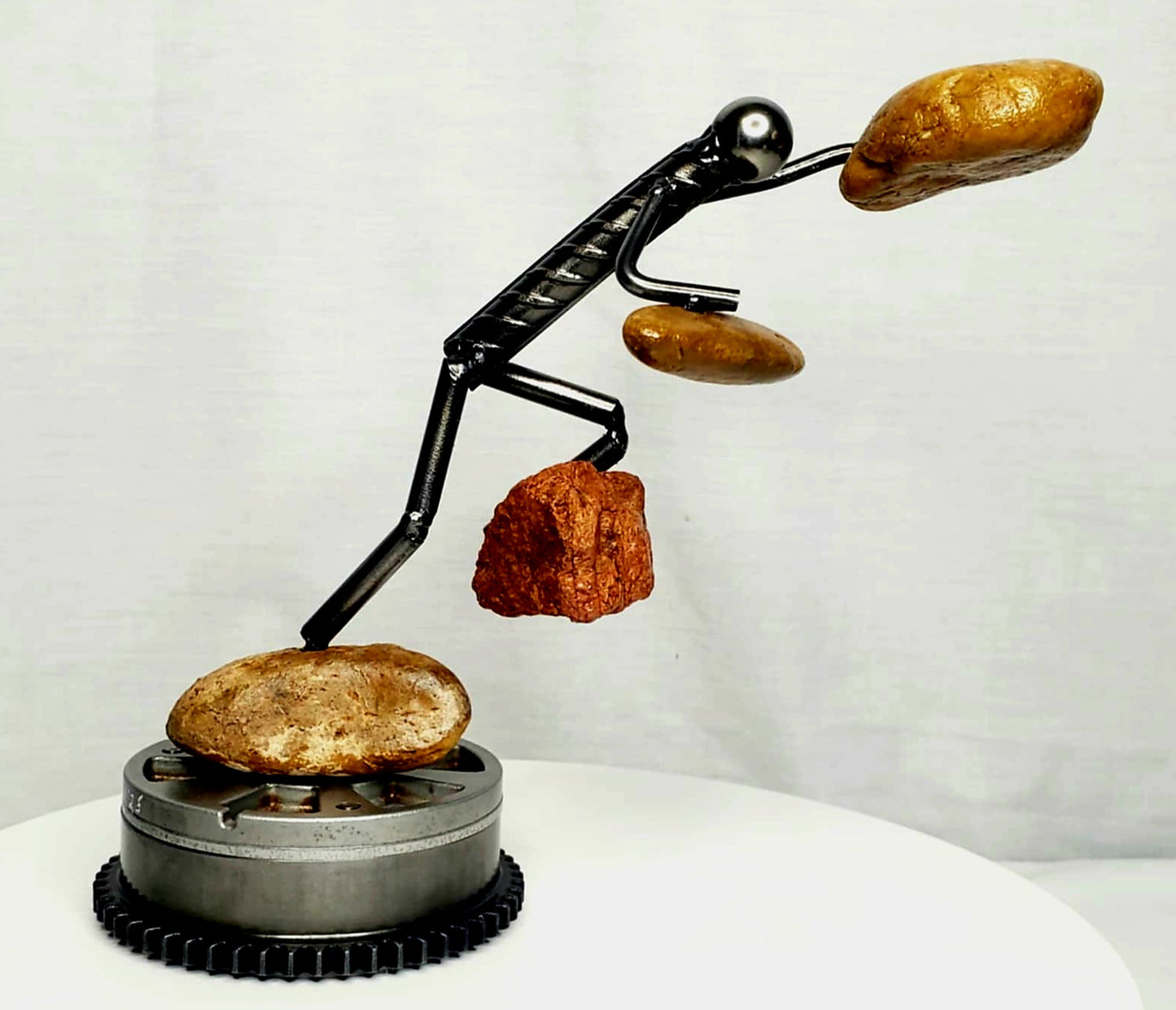 The Rock Climber welded steel figure scaling a natural stone peak sculpture by Enrique Del Angel handcrafted from upcycled auto parts
