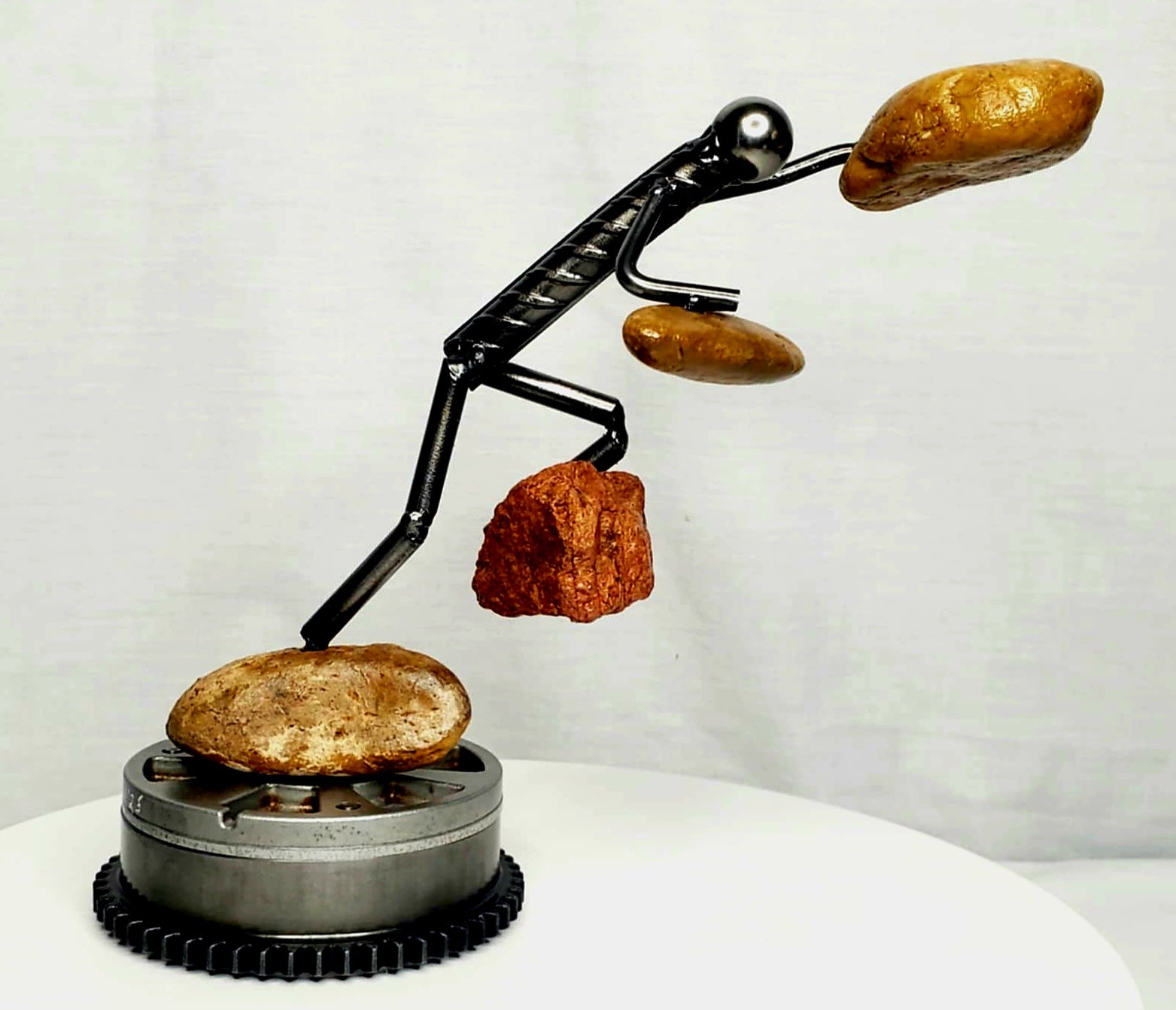 The Rock Climber welded steel figure scaling a natural stone peak sculpture by Enrique Del Angel handcrafted from upcycled auto parts