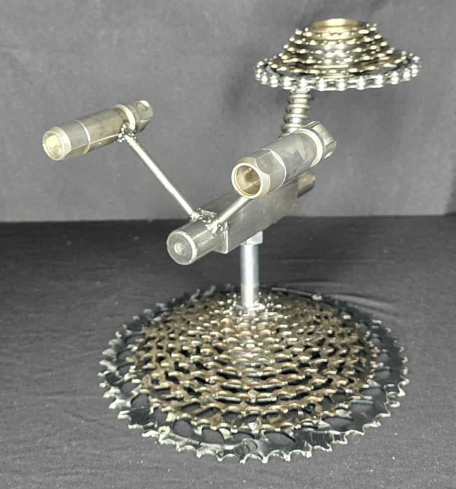 Welded steel rocket sculpture by Enrique Del Angel, resembling the U.S.S. Enterprise, with bicycle gears for base and saucer.