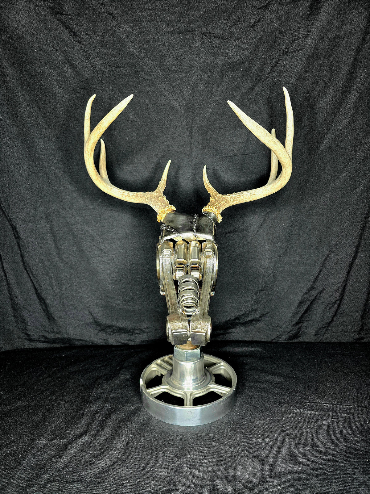Torque & Tines sculpture by Enrique Del Angel: deer skull made of engine parts with real antlers on a pulley wheel base.