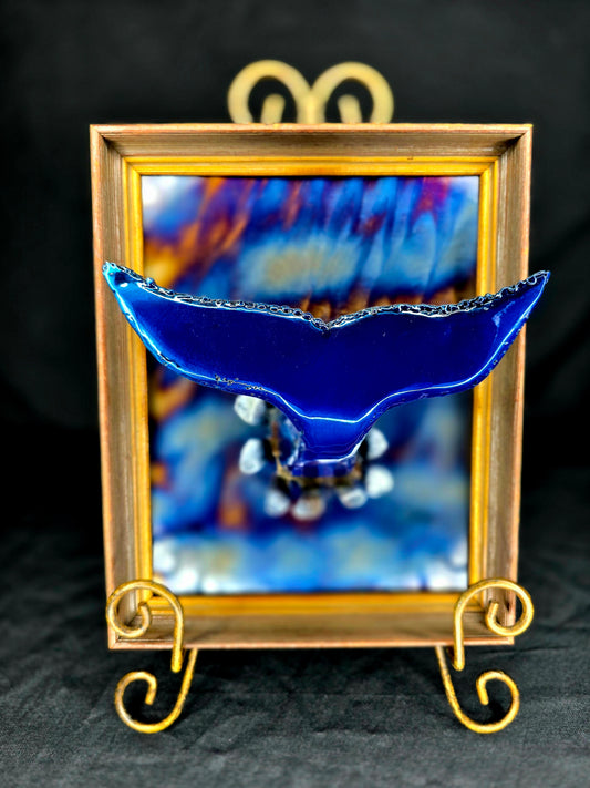 Whale Hello by Enrique Del Angel, a blue metal whale tail sculpture displayed in front of a framed artwork.
